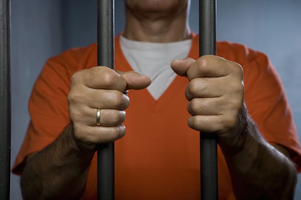 a prisoner standing behind prison bars 83678087 5764a5d73df78ca6e42cfe17